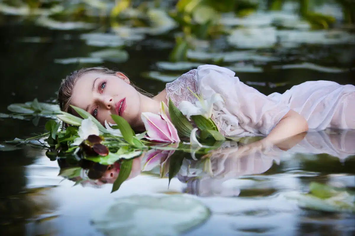a beautiful nymph lying in the water in a white dress with a bouquet of lilies