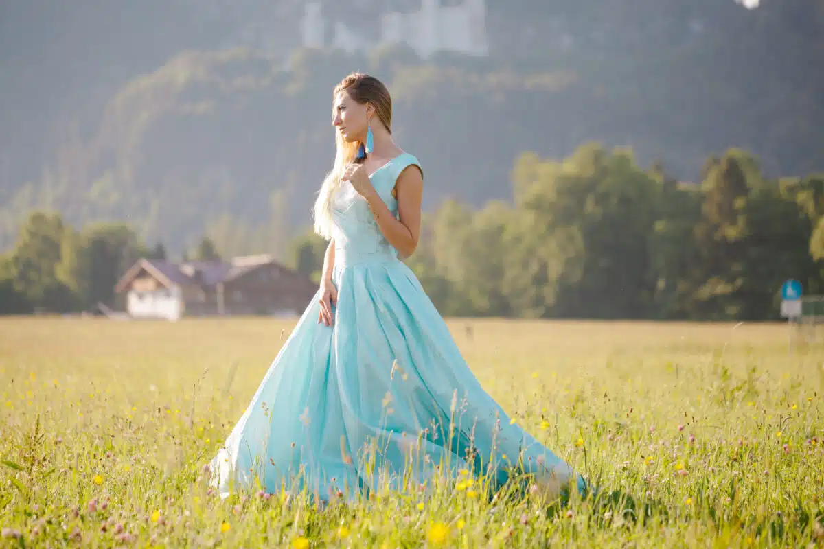 blond woman in blue dress enjoying outdoors in front of the castle
