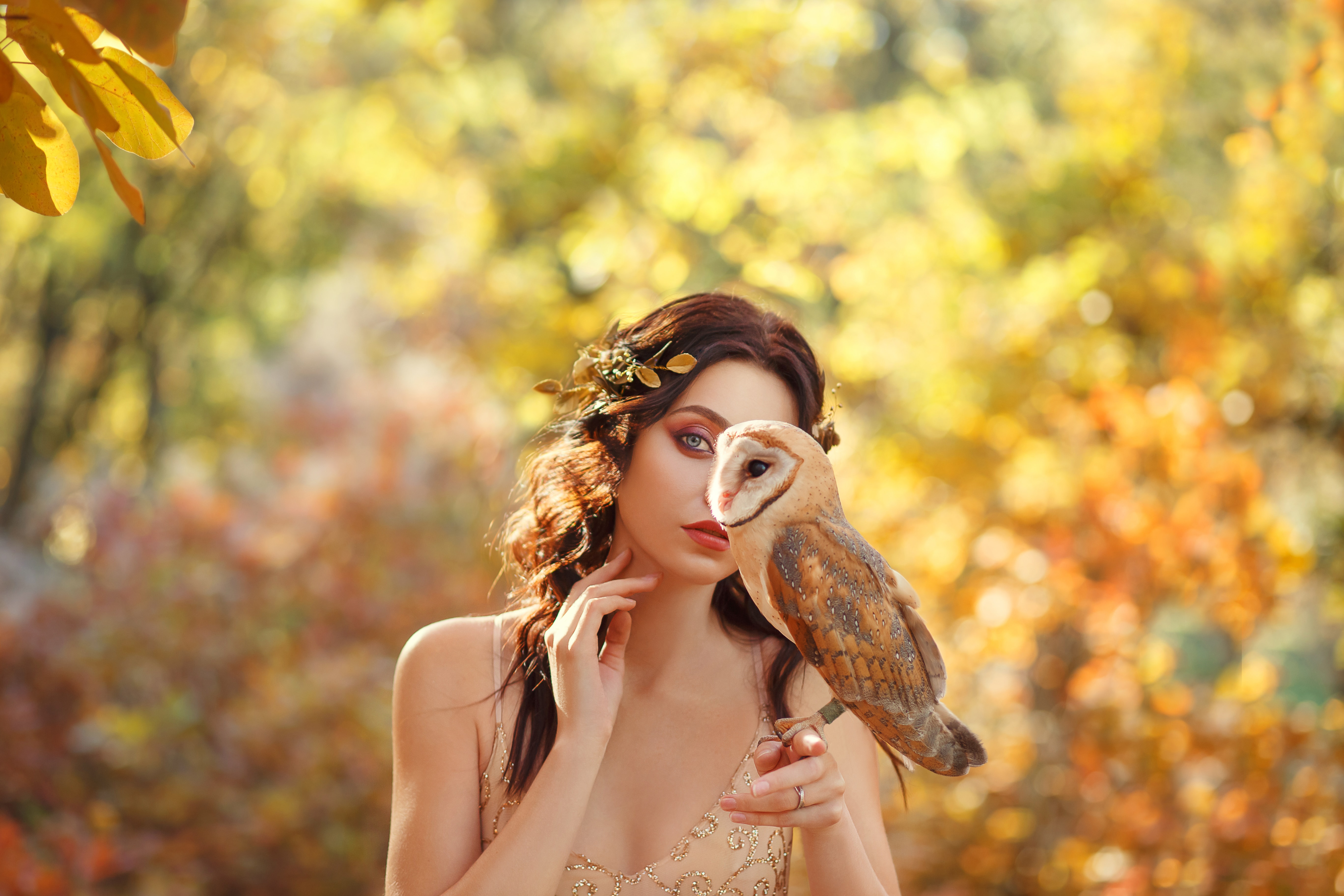 mysterious girl hides part of face behind owl sitting on the finger of a dark-haired attractive lady, princess dressed in beige light elegant dress, bright nice photo, solitude and unity with nature