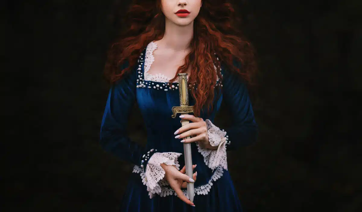 Fantasy woman warrior on black background, lady with red lips, long hair hands close up holding dagger, knife short sword. 