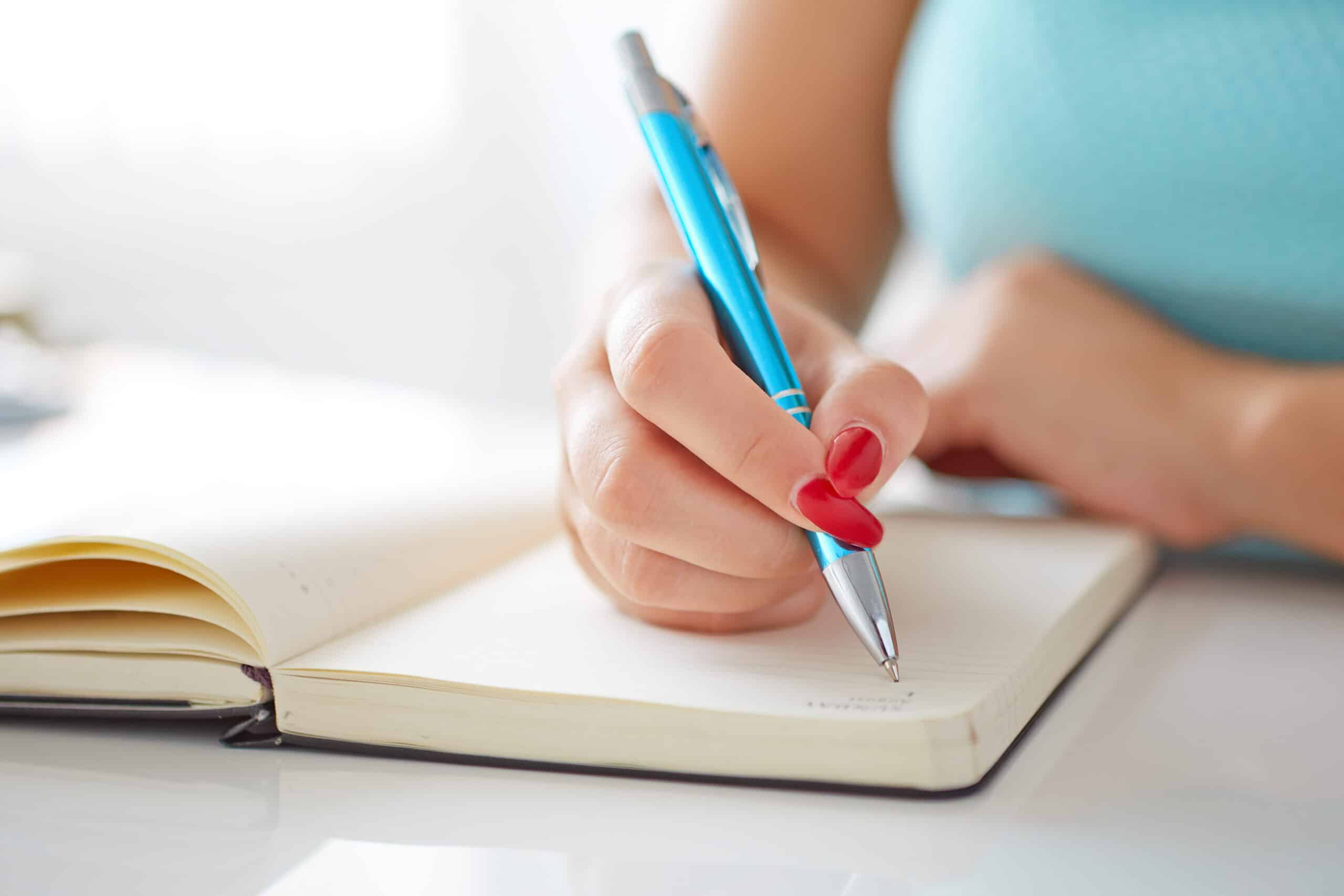 Young woman with red nail polish writes in her diary