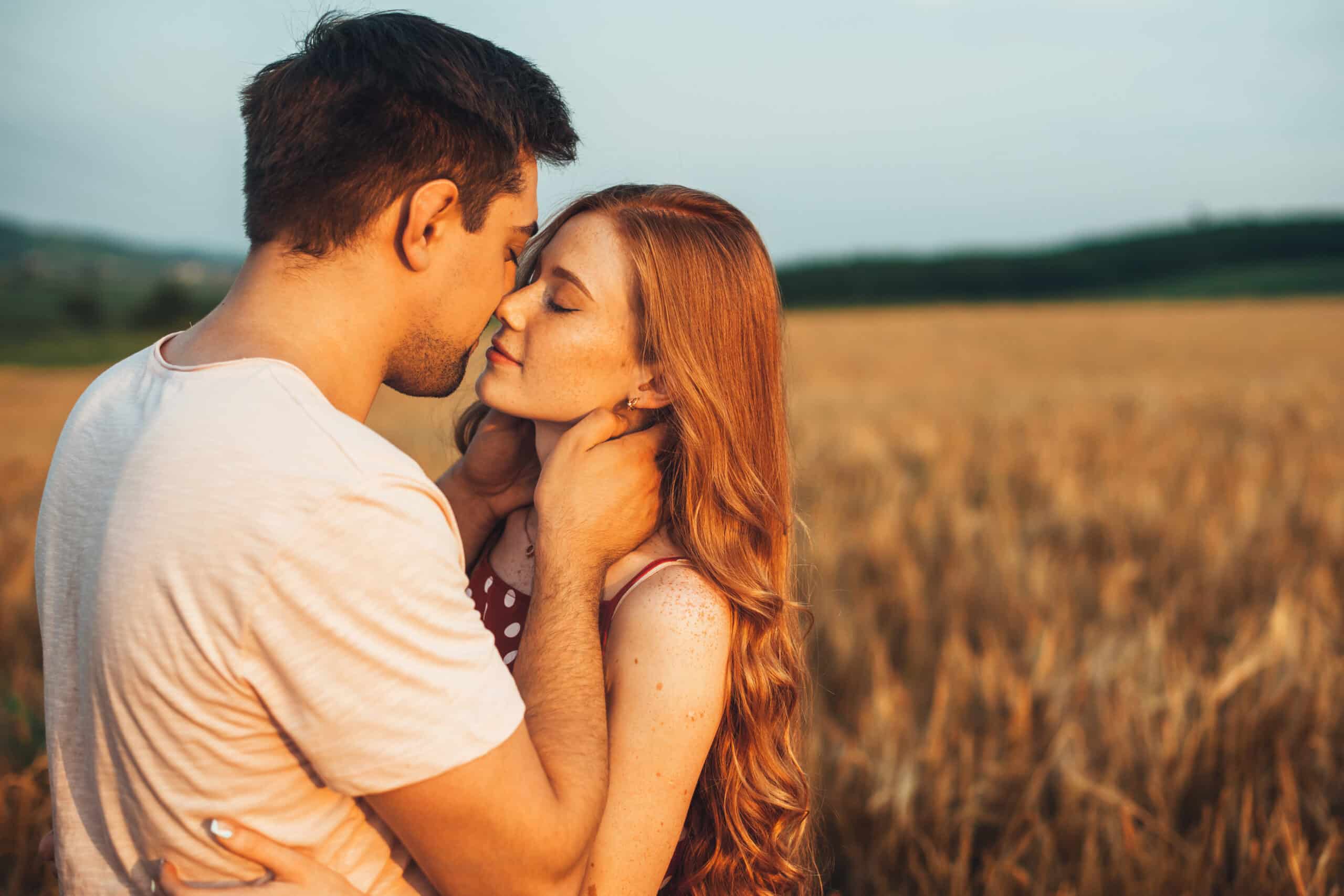 Caucasian couple kissing in the field of wheat on sunny summer day. 