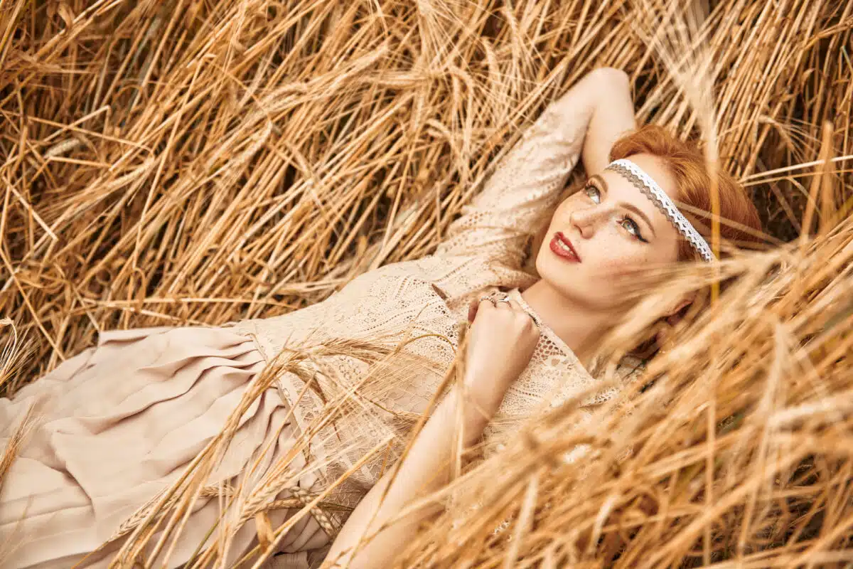 Romantic young woman with beautiful red hair lies on a wheat field