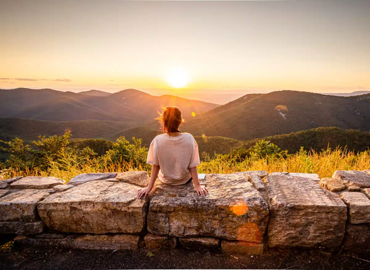 View of woman sees sunset over blue ridge mountains from skyline.