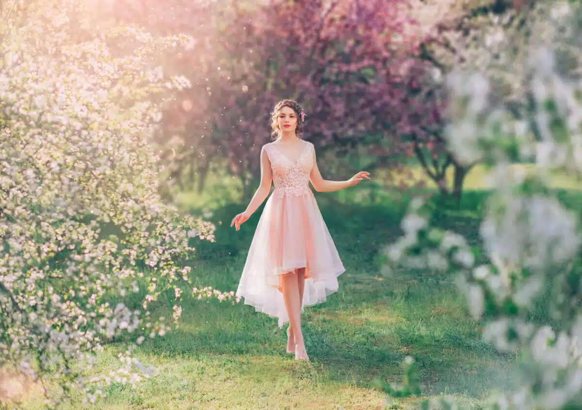 mysterious lady with dark hair in a light delicate peach dress walks in the blooming garden in spring