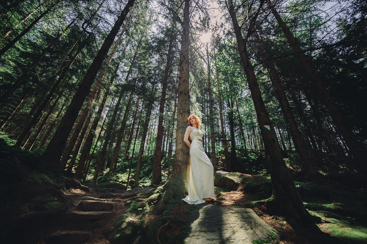 a young redhead in a white long dress in a green forest on summer day