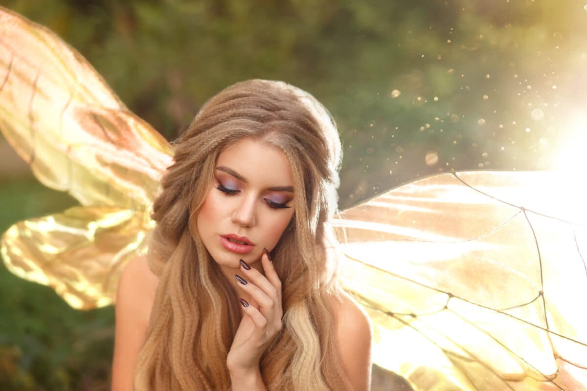 gorgeous young enchantress with transparent wings and blond hair with beautiful appearance, model posing with closed eyes, cool summer photo, fairytale hero with bare shoulders in the sun