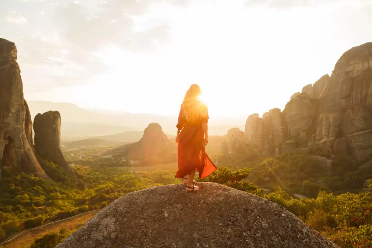 a maiden dressed in flowy red dress looking at majestic sunset in a valley