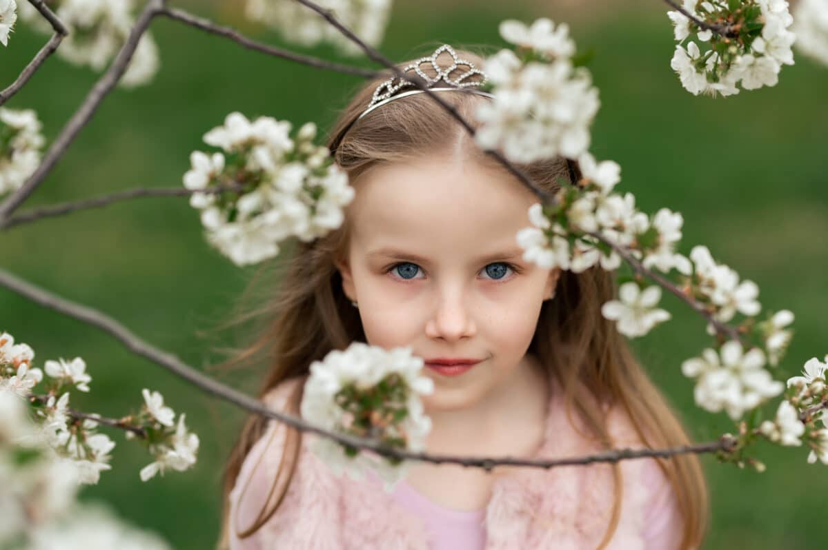 a beautiful little princess in a pink dress next to blooming tree