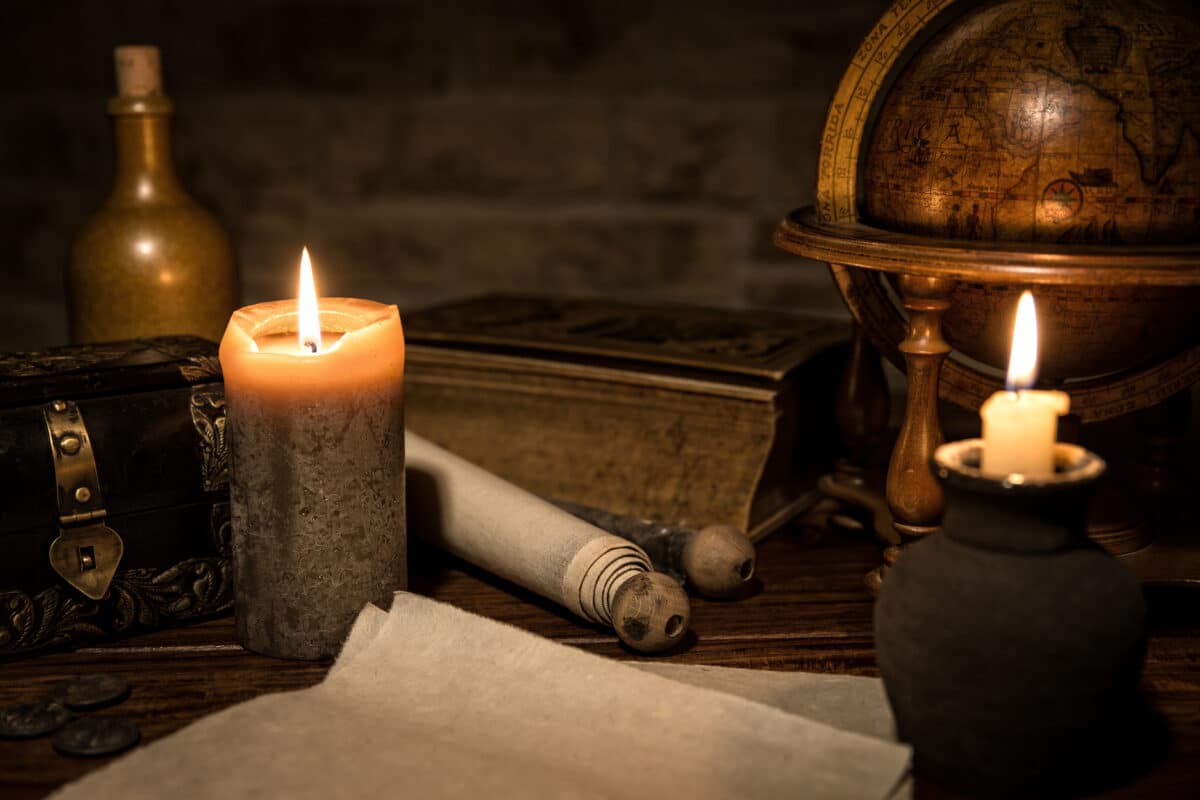 an ancient desk with candles, papers, and a vintage globe