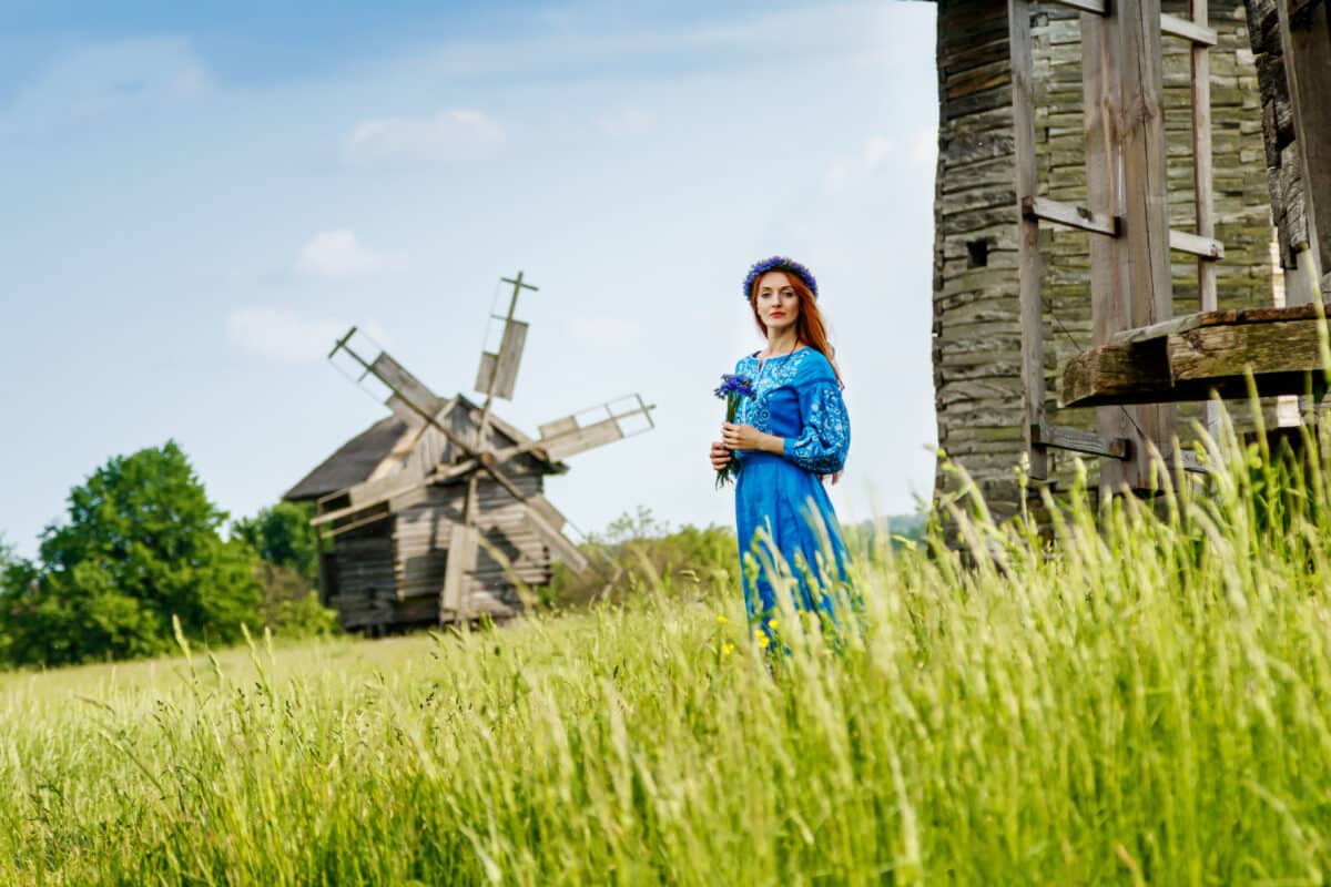 Beautiful red-haired maiden in a blue dress outdoor in the field of green grass