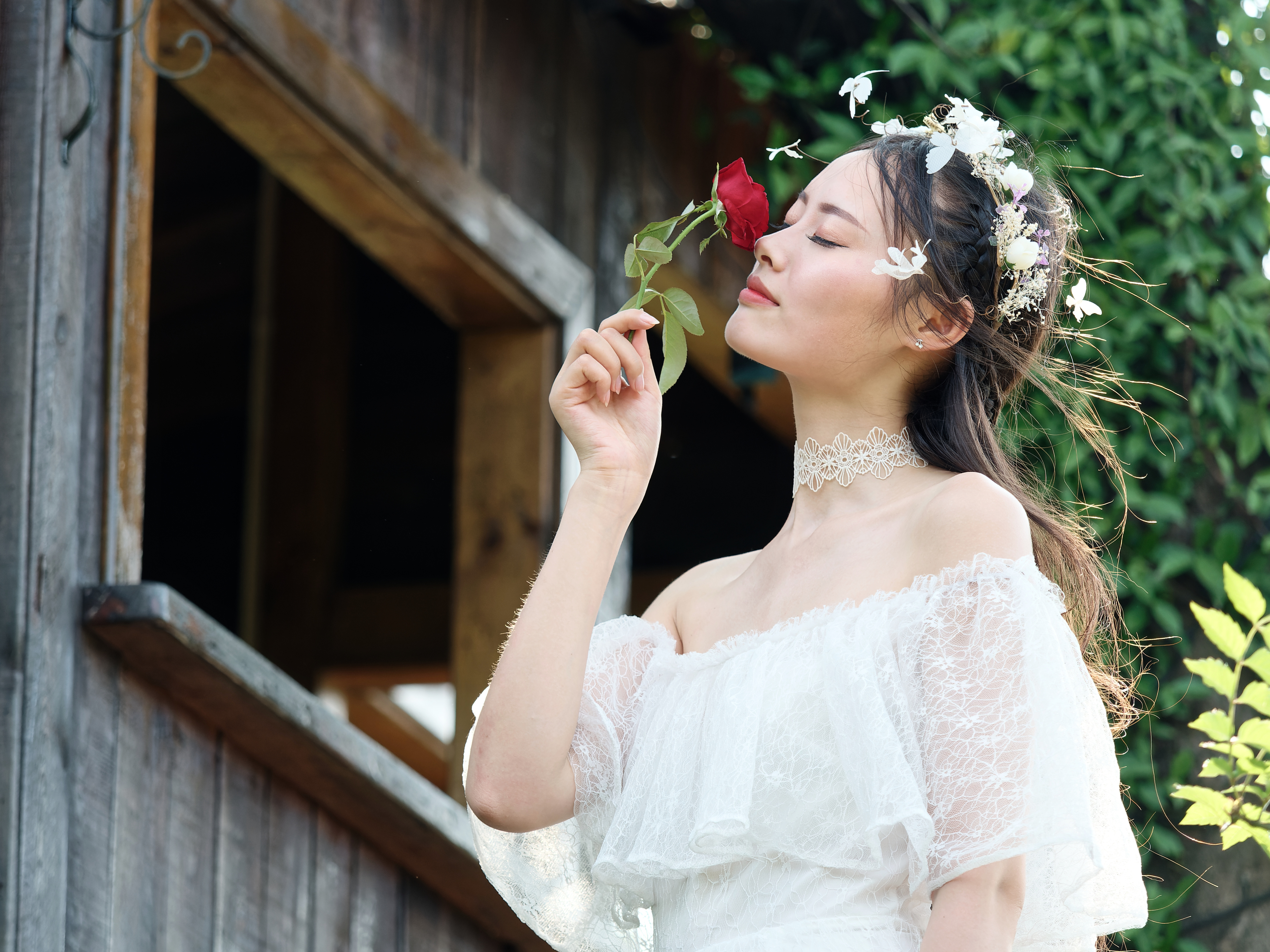 Beautiful young lady in white dress, eyes closed holding a rose to her face