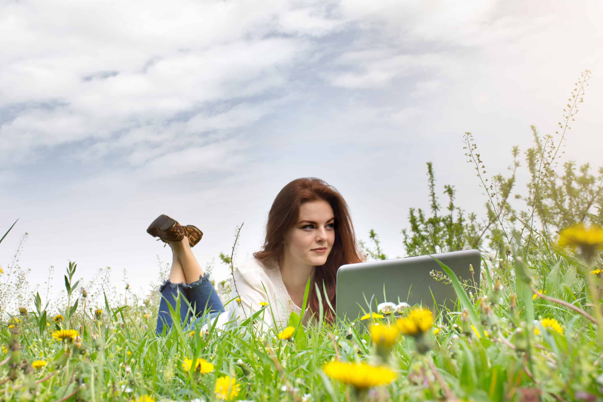 Redhead woman using laptop in the park lying on the green grass
