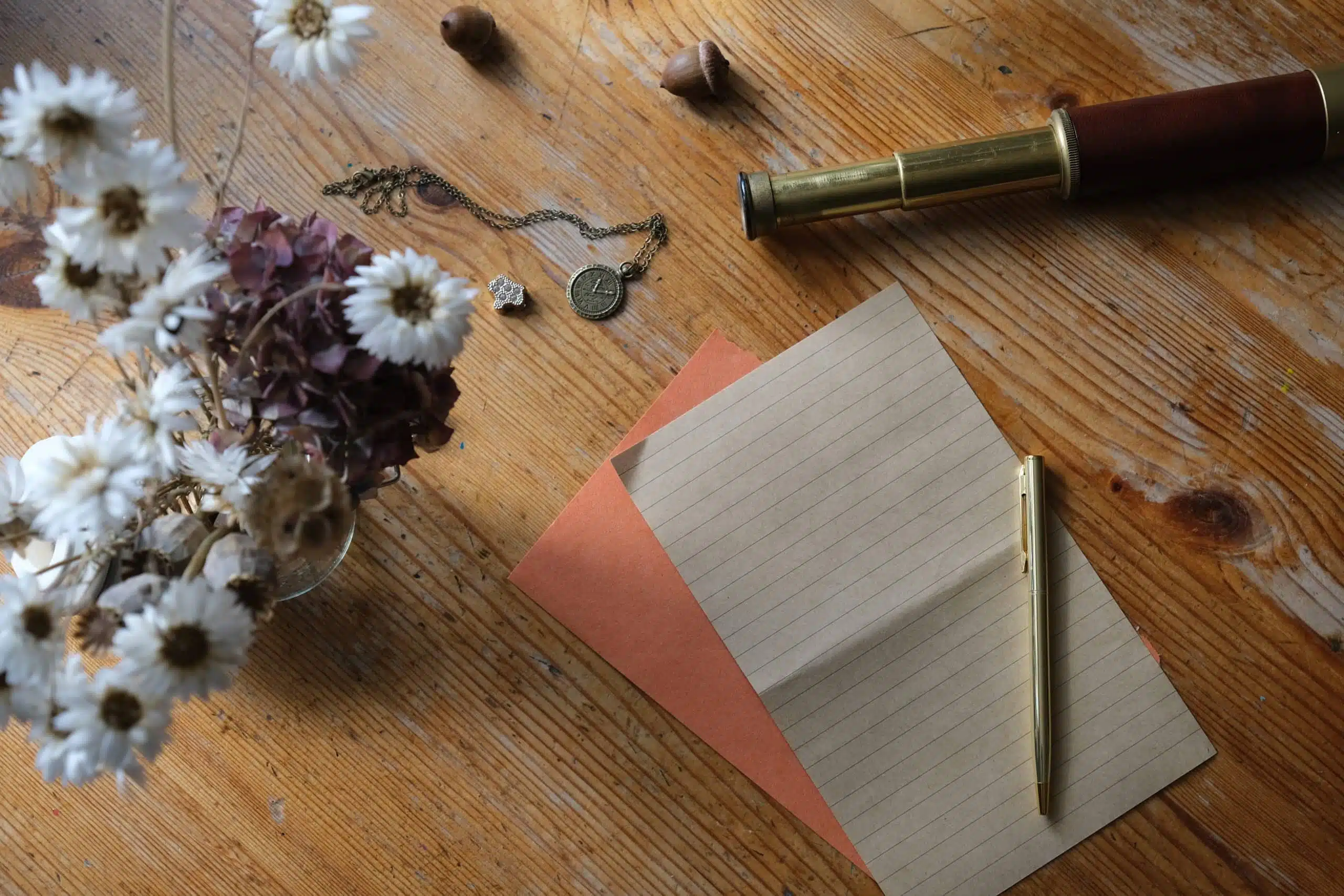 Vintage paper, pen and a vase of dried flowers on wooden desk.