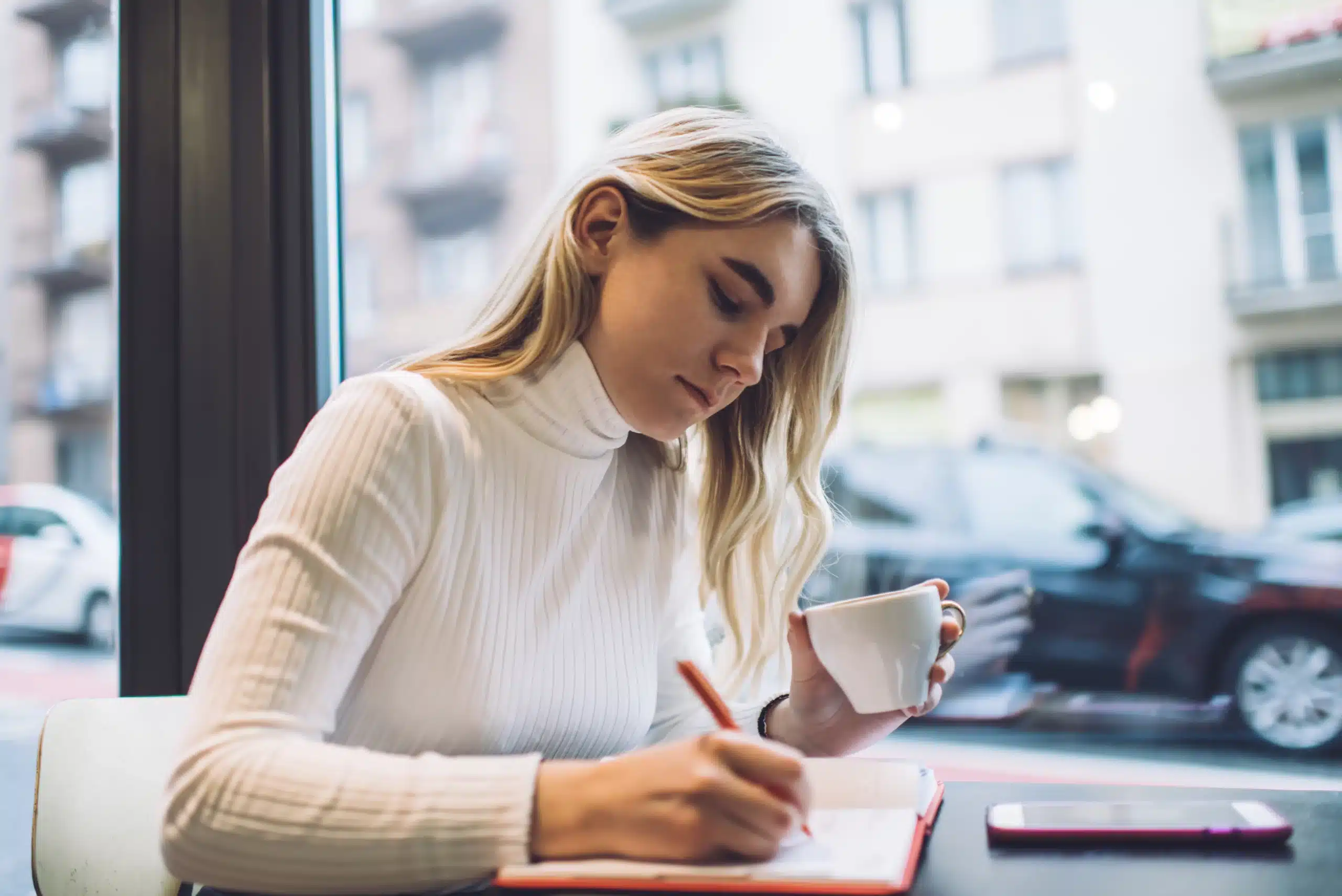 Serious woman with coffee writing in notepad