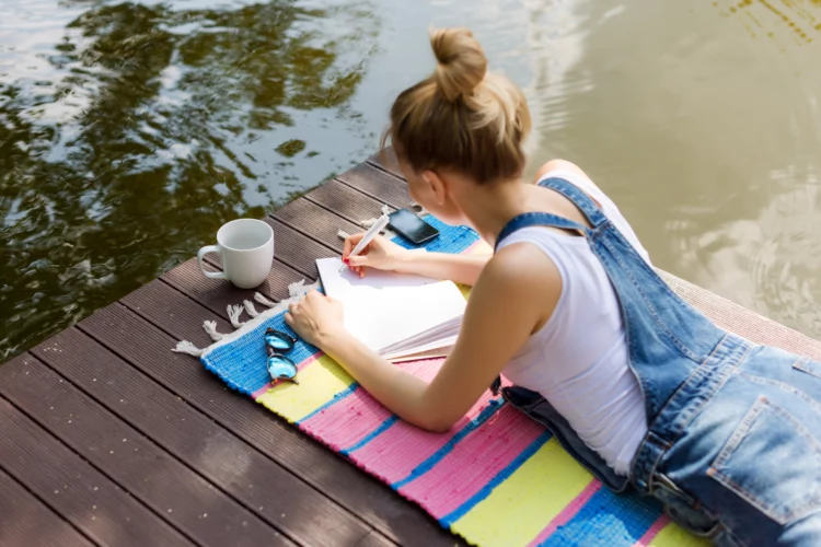 woman in casual clothes lying on wooden bridge writing in her diary 