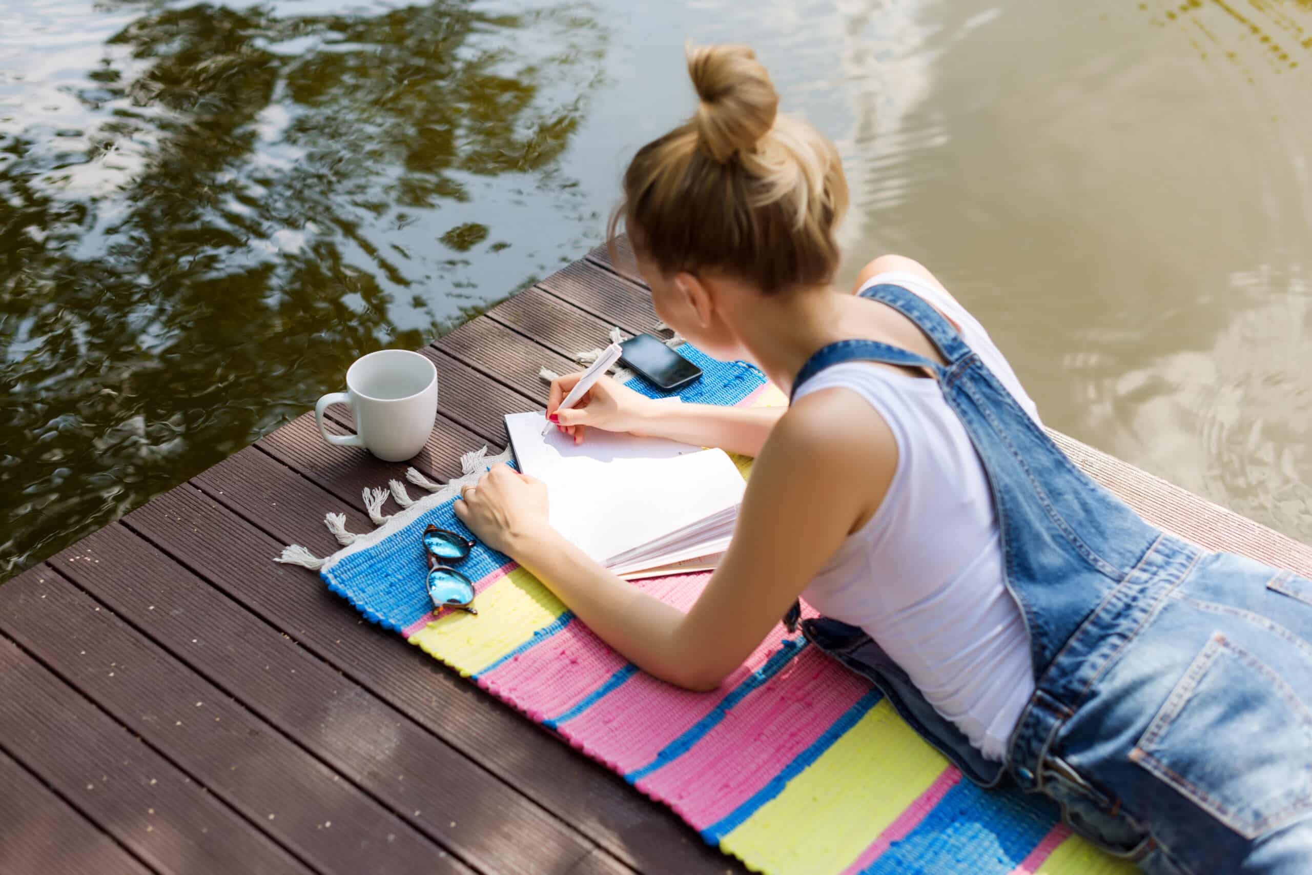 woman in casual clothes lying on wooden bridge writing in her diary