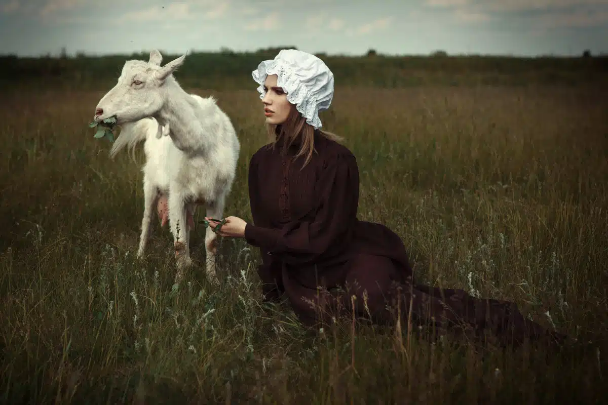 Beautiful country woman sitting on the grass with a white goat.