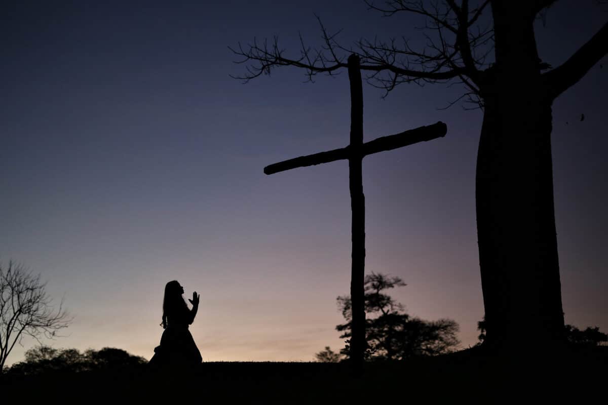 silhouette of a woman kneeling and praying with devotion and  love in front of the cross on the hill