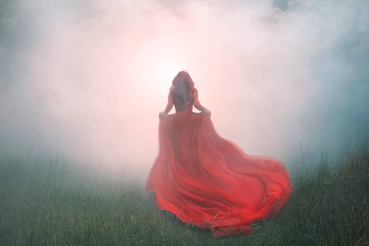 gorgeous amazing wonderful scarlet red dress with a long flying waving train, a mysterious girl with red curly hair runs away into a thick white mist and forest haze over the green summer grass