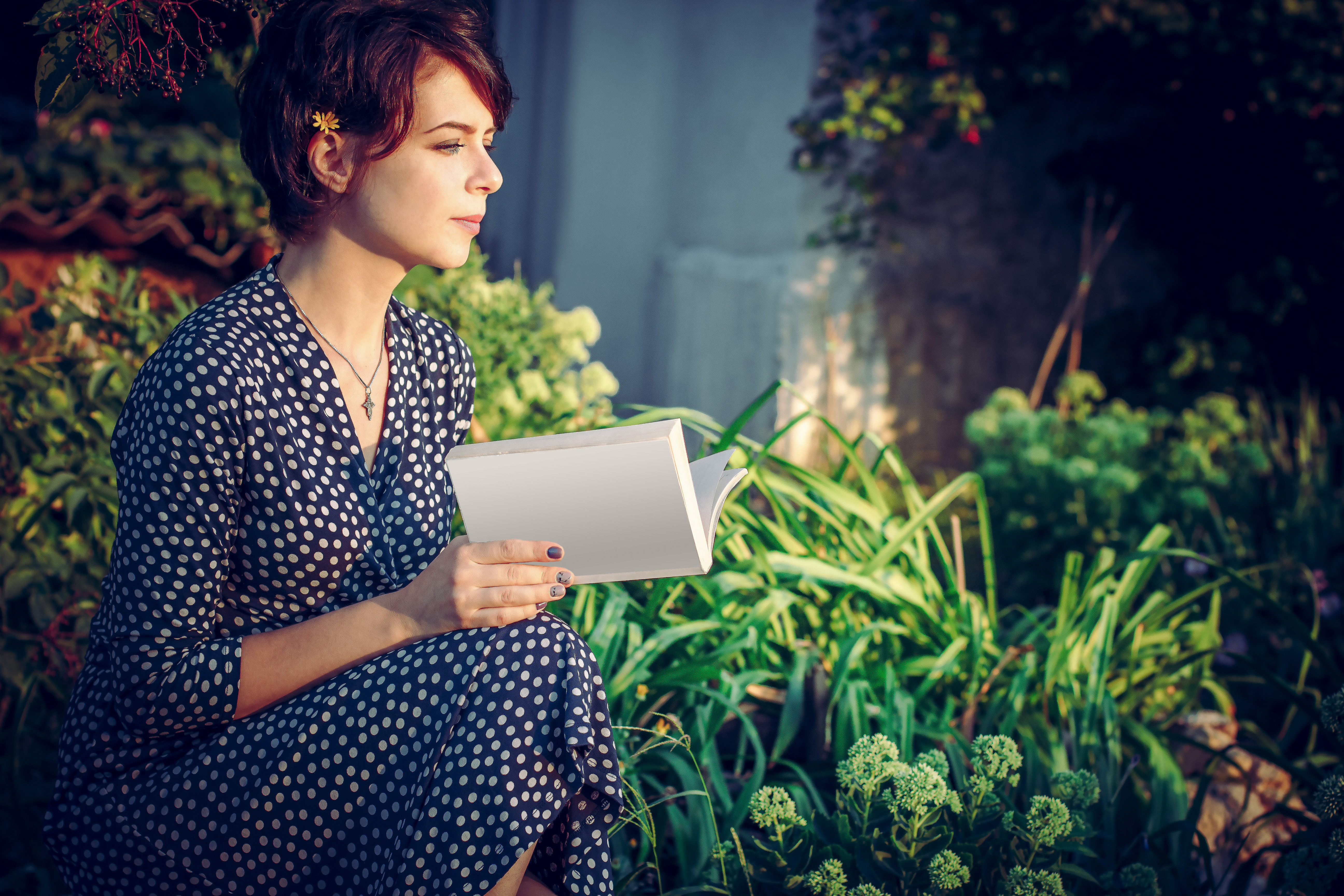pretty young woman holding a white diary sitting beside the plants
