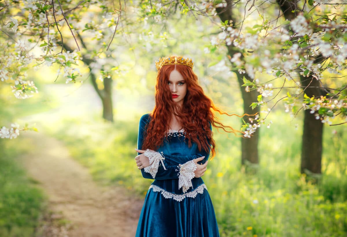 redhead princess with fierce look standing on a path in the woods