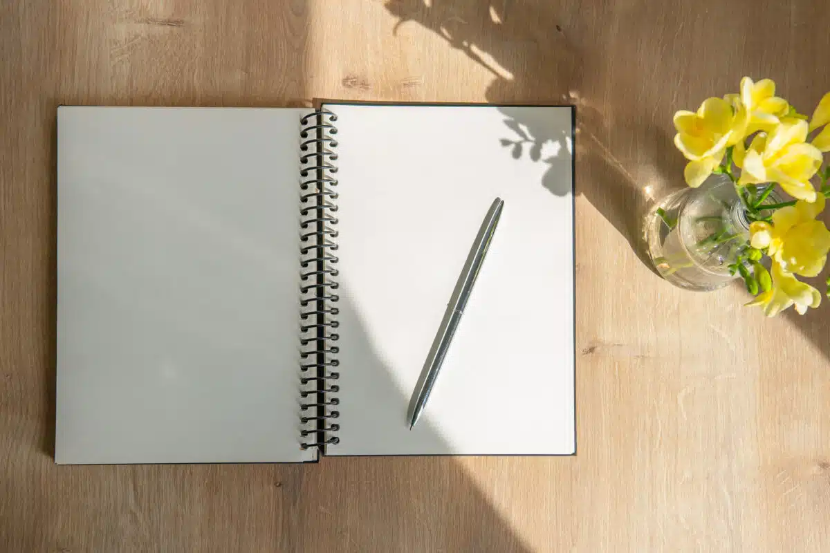 open notebook with pen and flowers on a wooden table. desktop top view