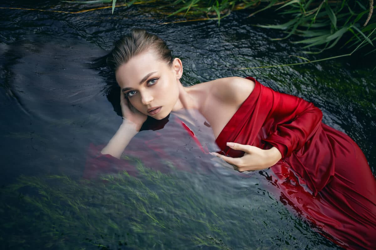 a beautiful romantic woman in a red dress lying in a green river 