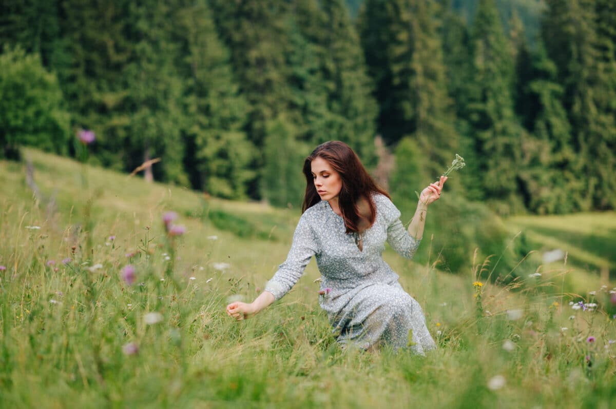 Pretty lady in a long blue dress collects flowers on a meadow in summer