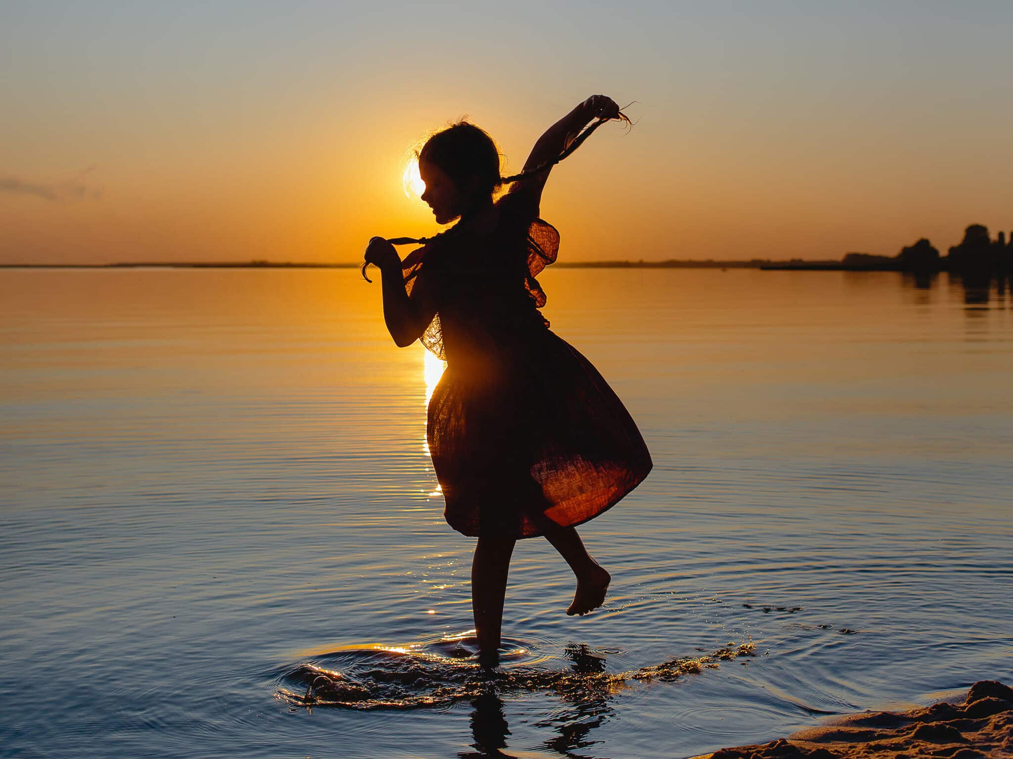 Silhouette of a dancing girl at sunset on the background of the river. 