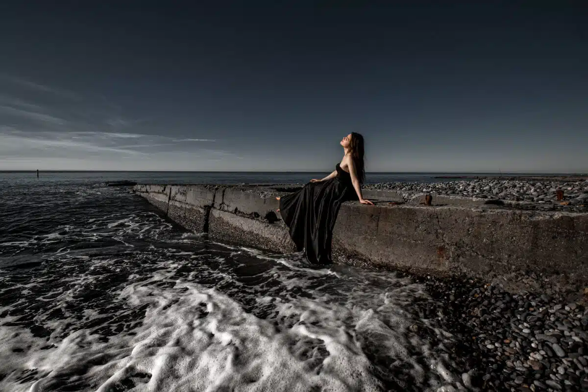 maiden in a black dress sitting on the seashore