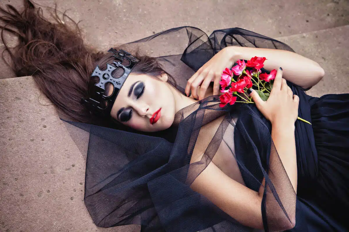 Dark queen in a veil and crown holding red flowers with closed eyes