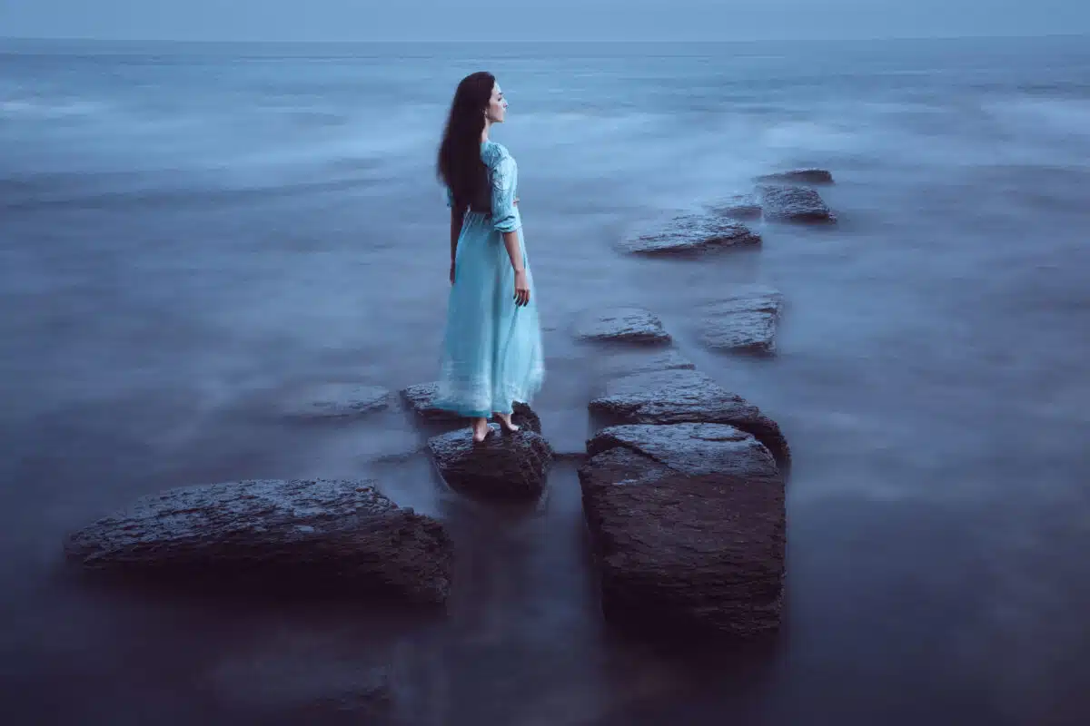 Beautiful but sad young woman walking on stone path in the dark sea
