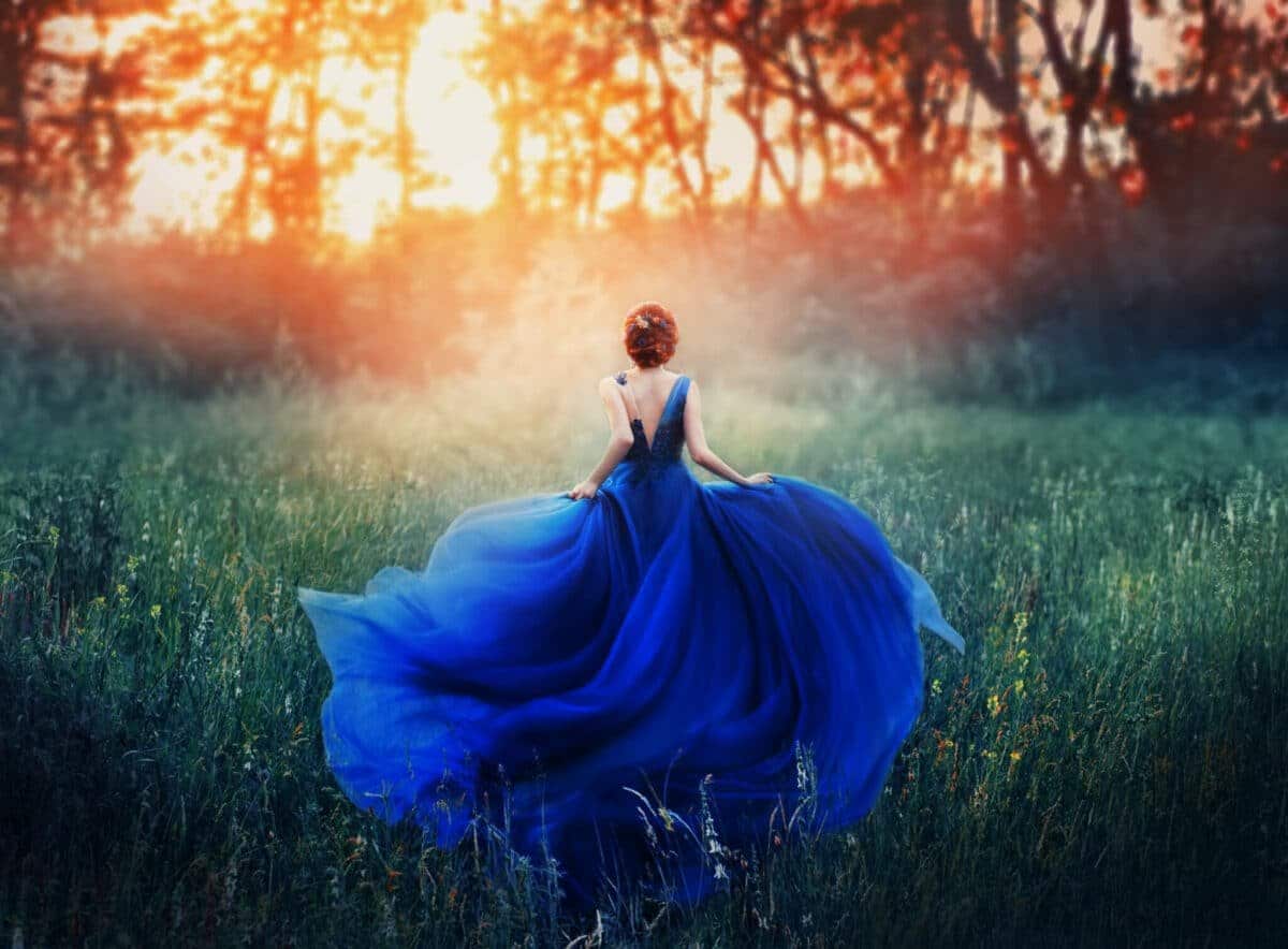 woman in a blue dress running to the sunset in the field of green grass