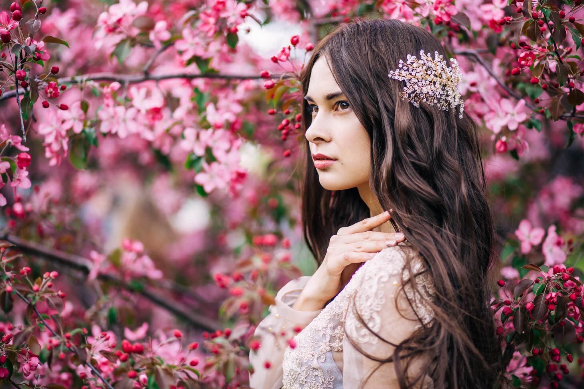 beautiful brunette girl in transparent dress, with decoration on the hair, near the tree blossoms with pink flowers