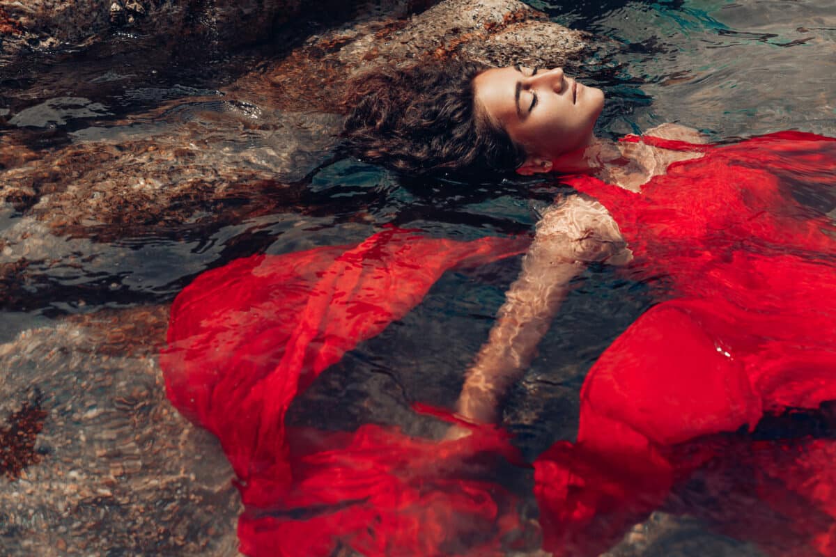 beautiful young woman in red dress lying in the water with eyes closed