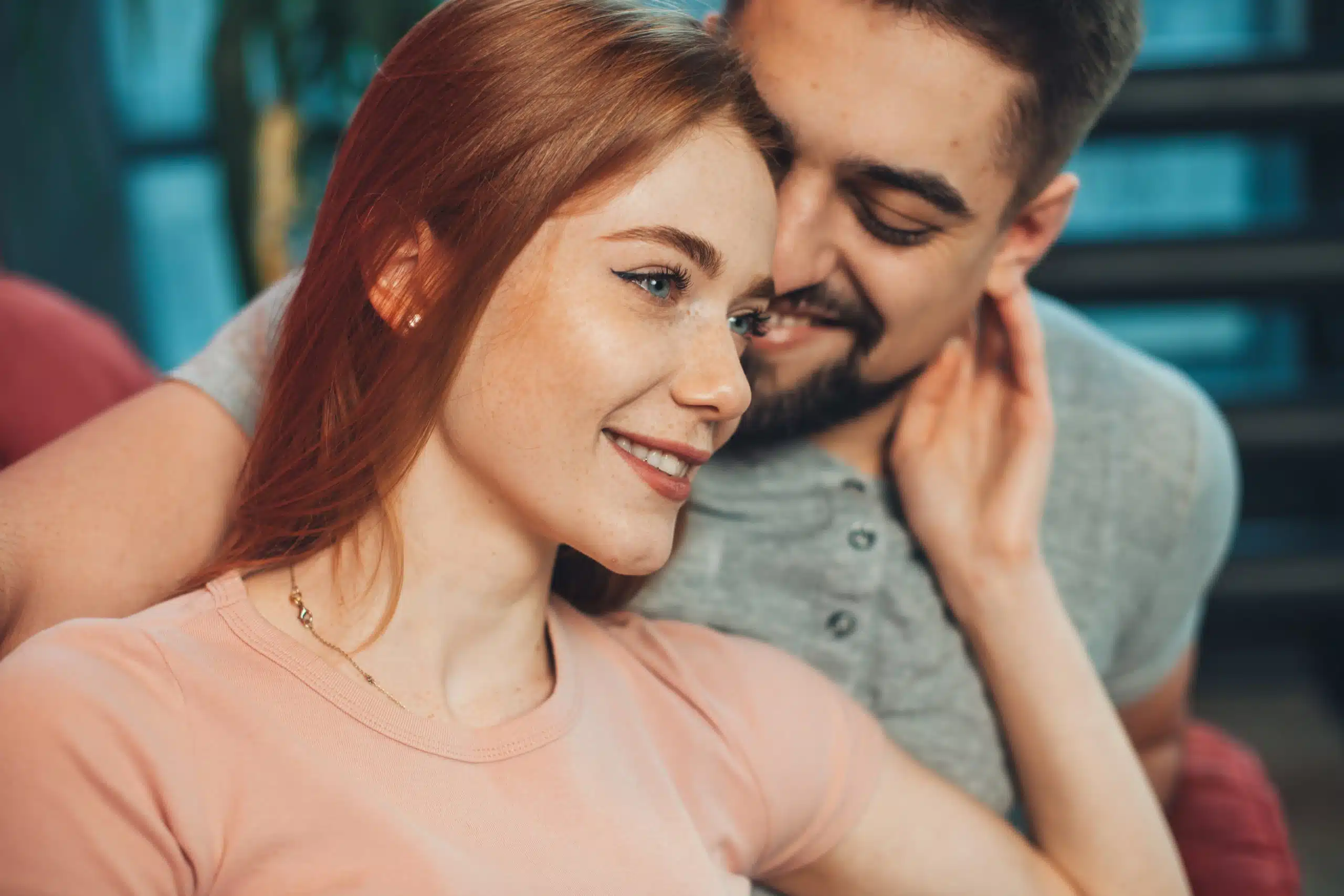 Attractive couple sitting on the couch on the weekend, freckled woman with red hair touching her husband's face.