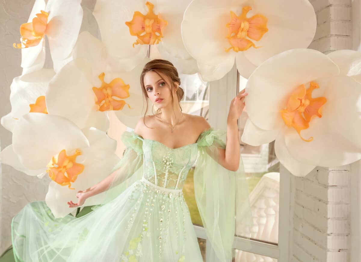 A beautiful young tender girl in an evening long green dress stands with large white orchids
