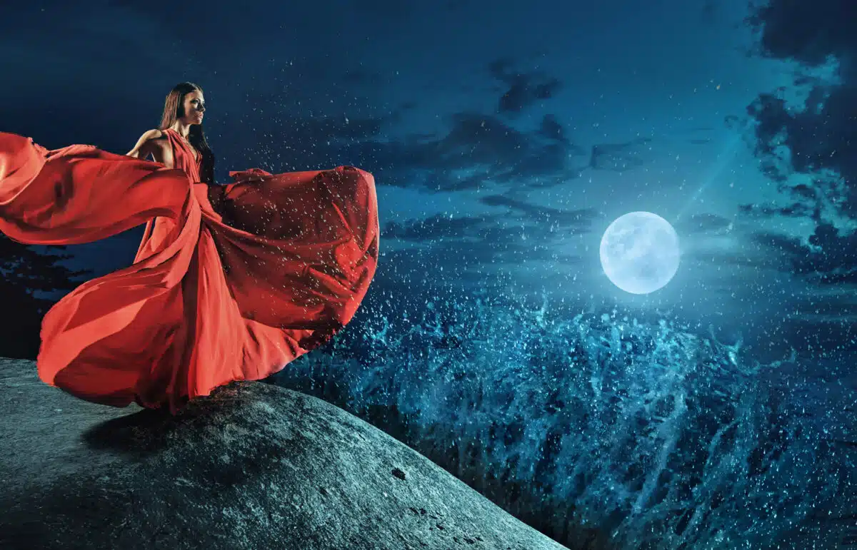 Beautiful lady in a red dress looking at the storm on the ocean
