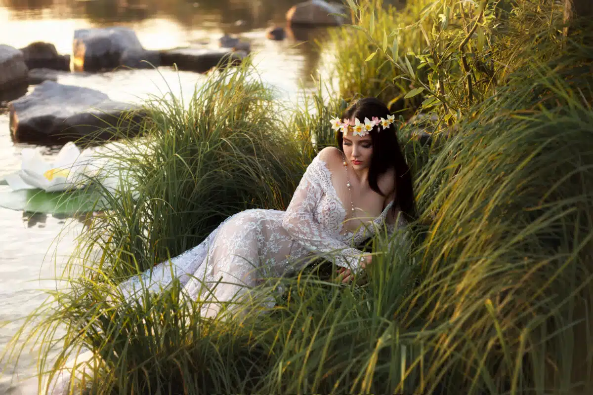 Luxurious lady, in elegant long dress lying on shore of lake