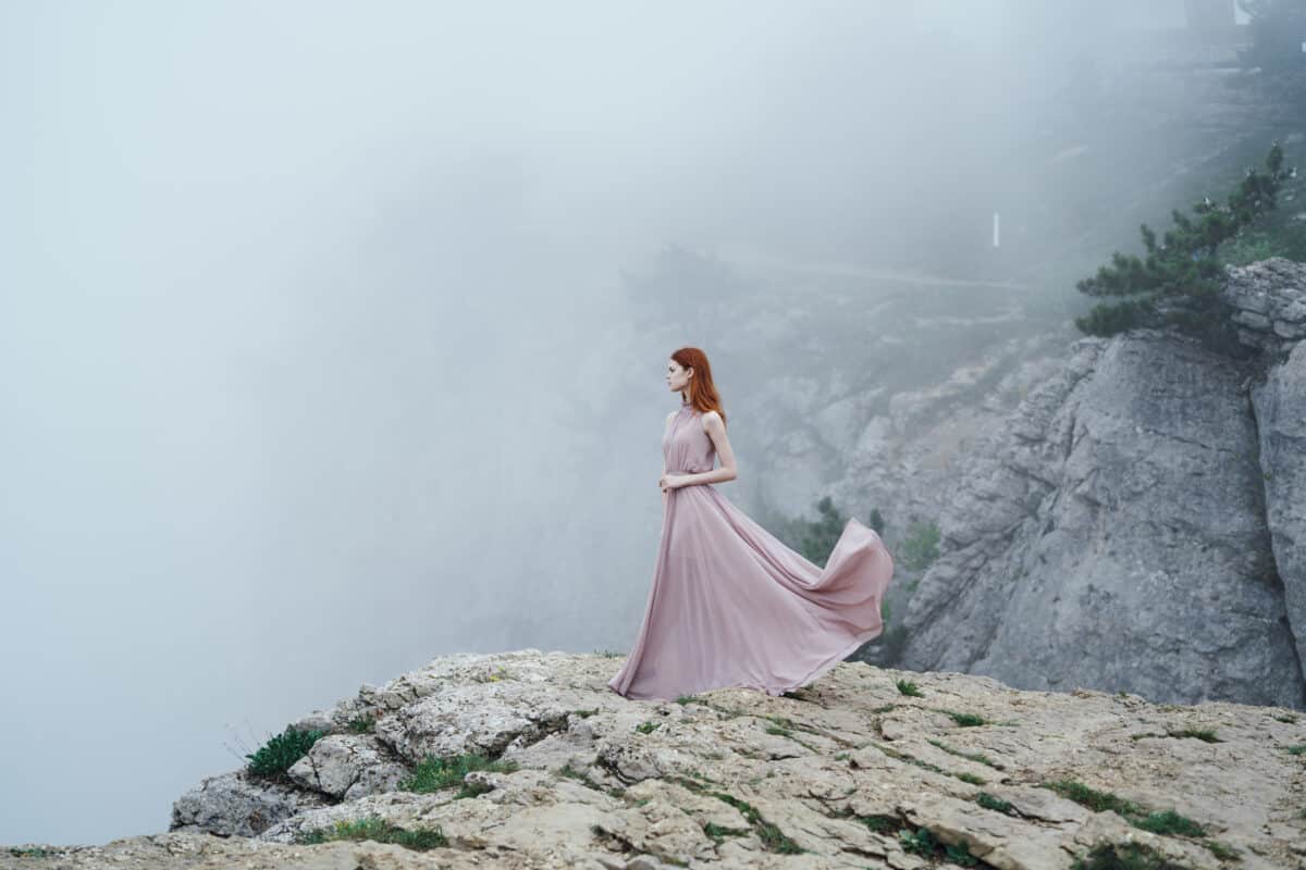 lonely sad woman in a long pink dress in the fog in the mountains