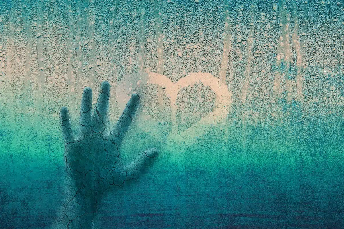 Cracked human hand on window with heart sign