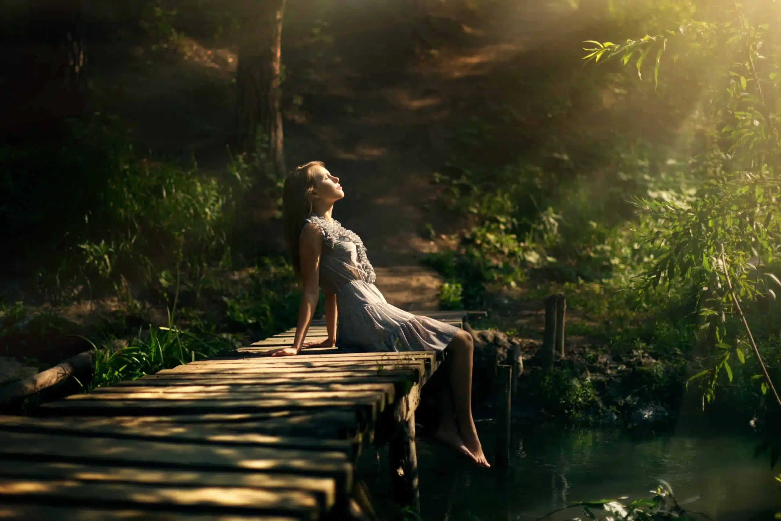 Beautiful girl sitting on an old wooden bridge in the green forest.