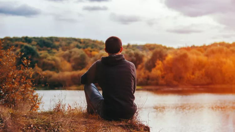 a lonely young man sitting on the shore in autumn