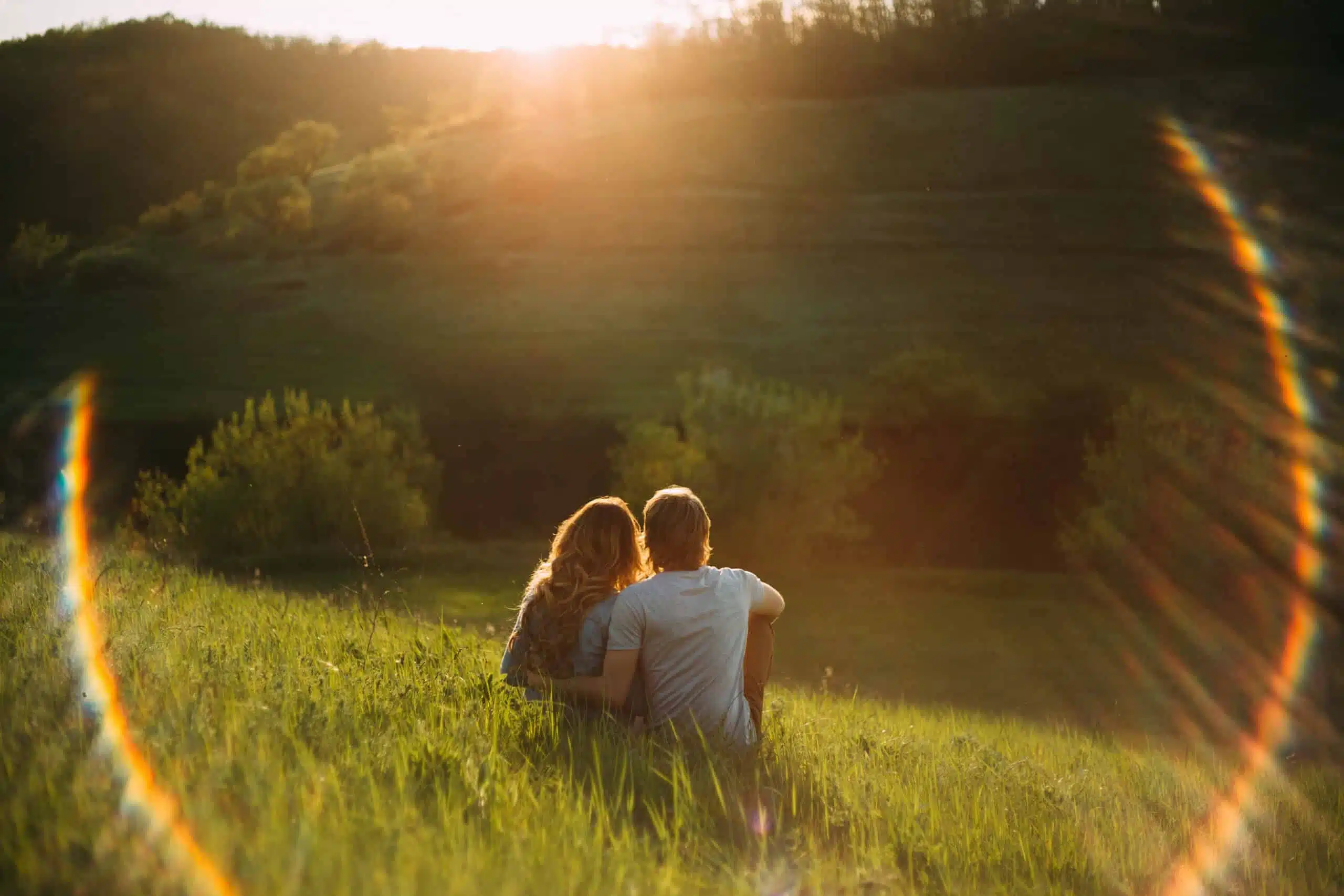 Stylish young couple sitting on a hill and admiring the sunset