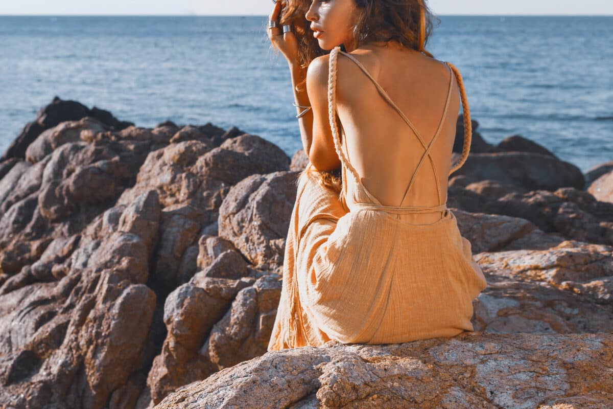 
beautiful young woman sitting on the stone by the sea at sunset