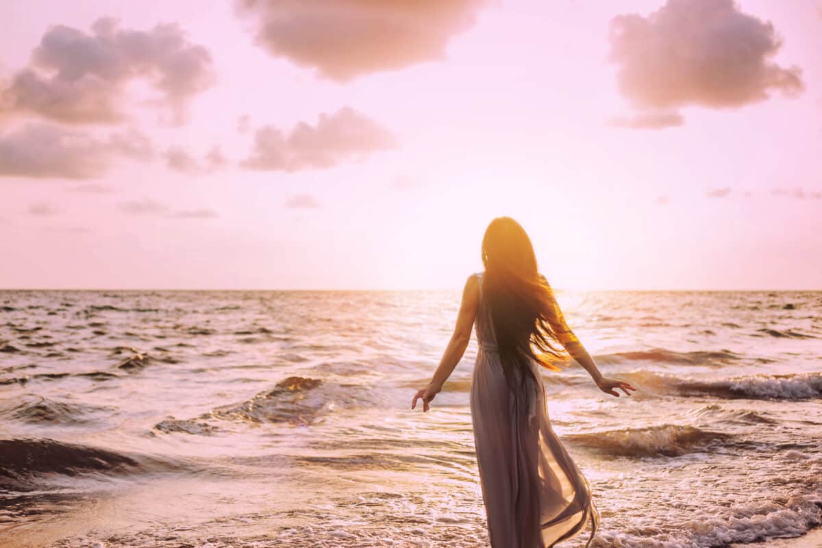 Art dark mysterious silhouette woman on sea shore nature air. Meditation prayer spiritual blessing divine calm. Summer Sun light. Happy Young princess long dress hair fluttering. back View. joy travel
