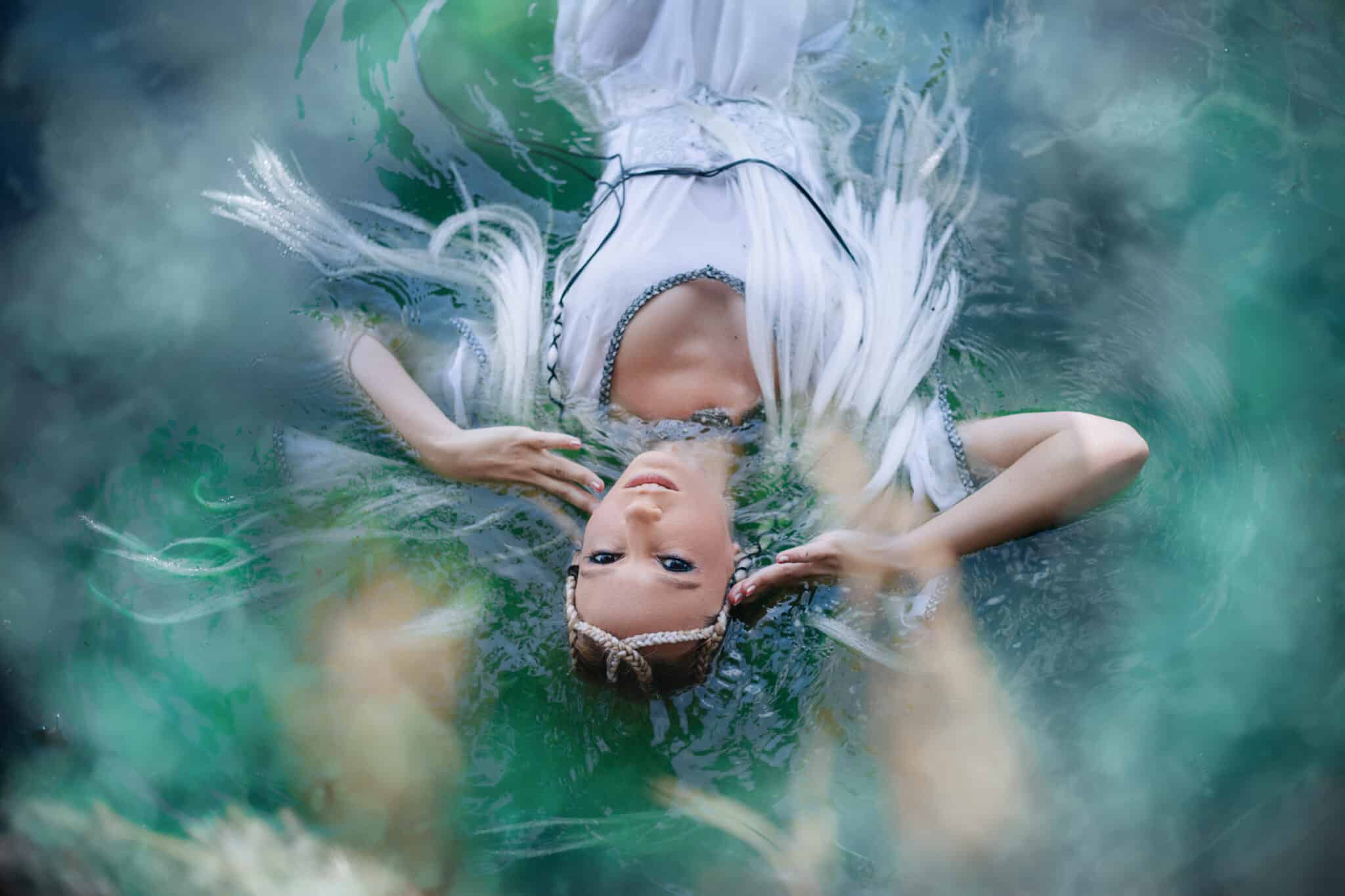 A girl elf in a white dress is floating in the water. 