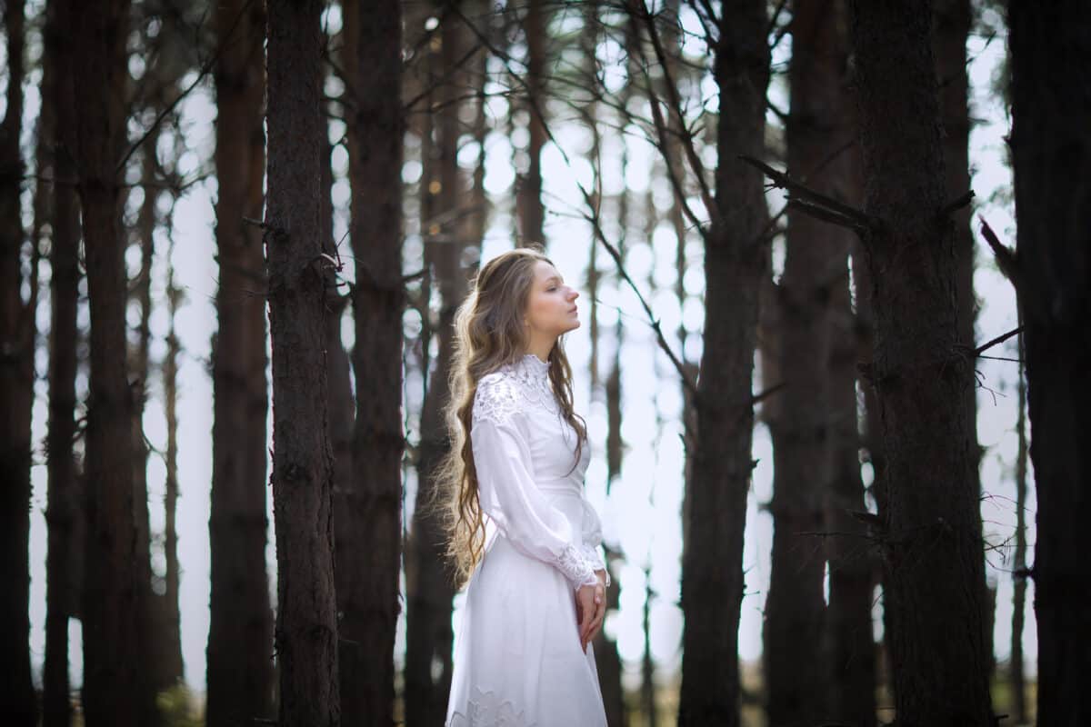 a lonely girl in a vintage dress walks in a dark forest
