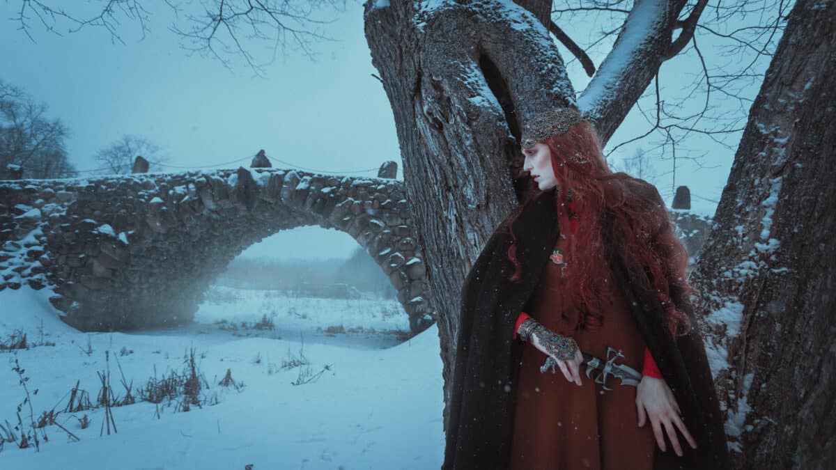 woman warrior in a medieval, fantasy costume, with weapons walking old Park, stone bridge in the winter. Winter is coming.